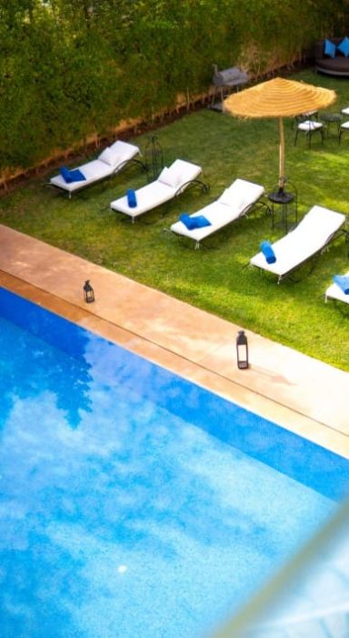 Chaises longues blanches autour d'une piscine, avec un parasol au-dessus, sur une pelouse verte.