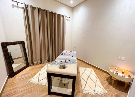 Salle de massage avec table, miroir, rideaux, tapis, et bougies décoratives.