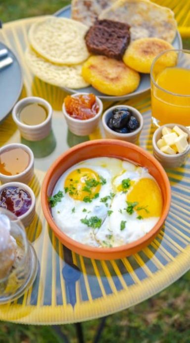 Petit-déjeuner coloré avec œufs, sauces, fruits et boissons sur une table en extérieur.