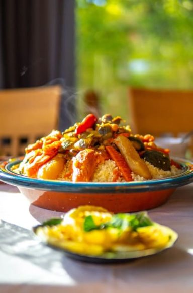 Un plat de couscous avec légumes colorés et sauce, accompagné d'une assiette de salade.